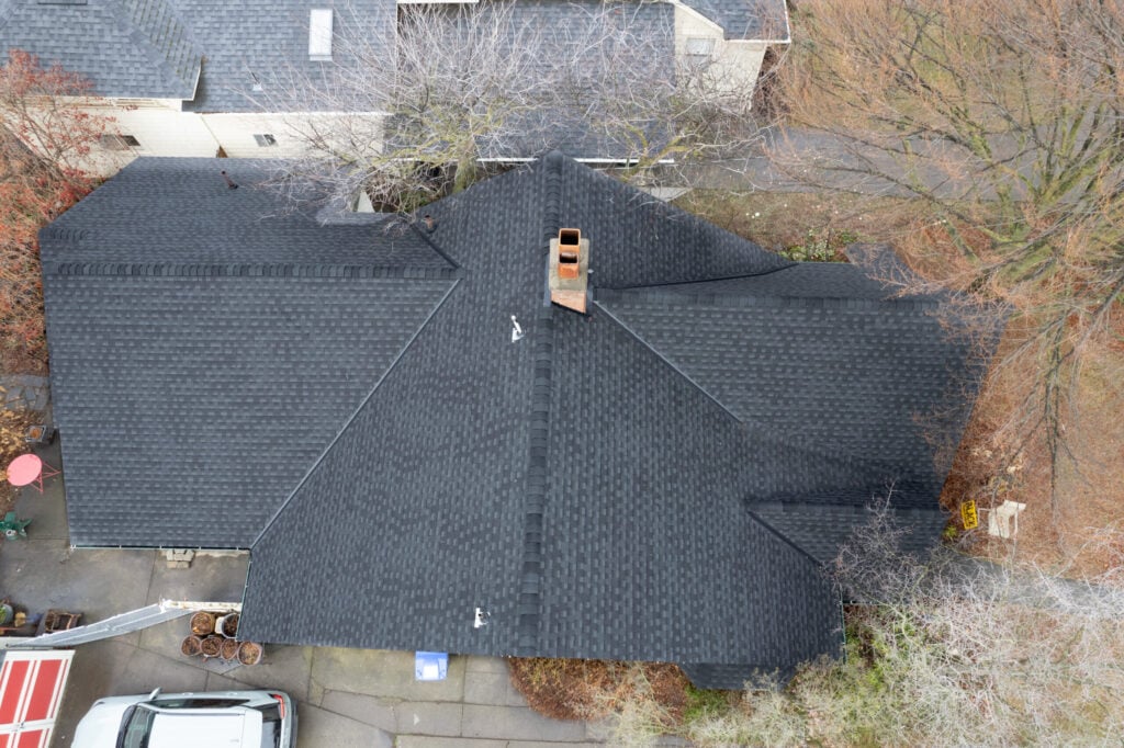 drone shot of black shingle roof surrounded by empty trees