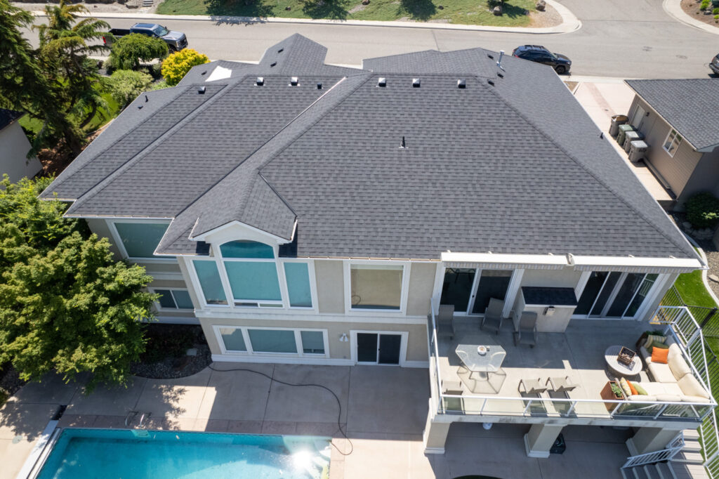 large home with black and gray shingle roof and pool with large deck