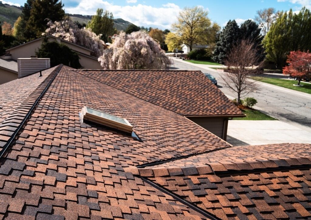 Brown and tan asphalt shingle roof on a street with trees