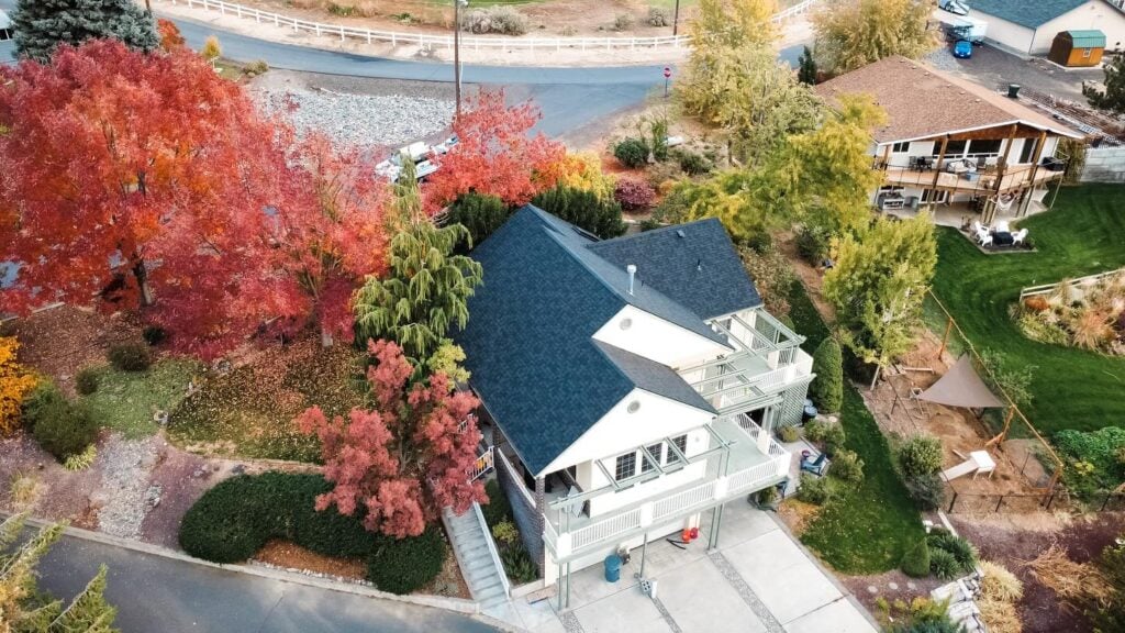 Big house with dark shingle roof surrounded by fall foliage