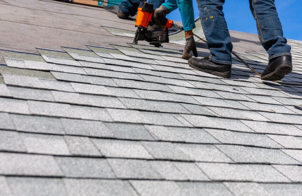 roofer installing asphalt shingles with nail gun