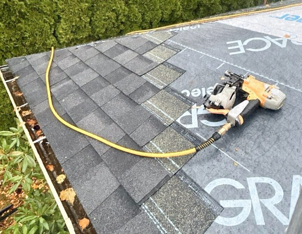 A nail gun laying on a roof with shingles being installed