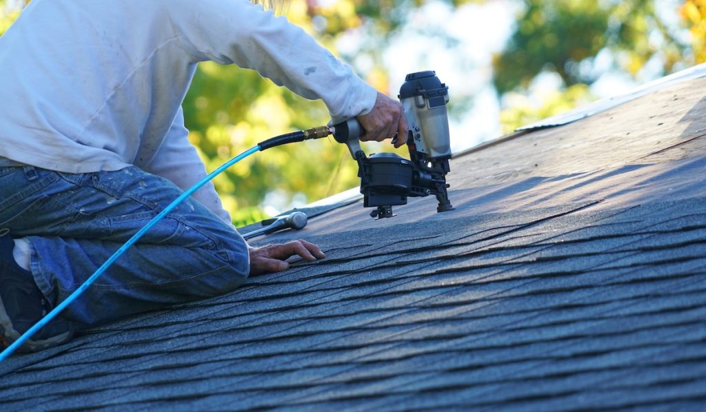 Worker with nailgun, adding shingles