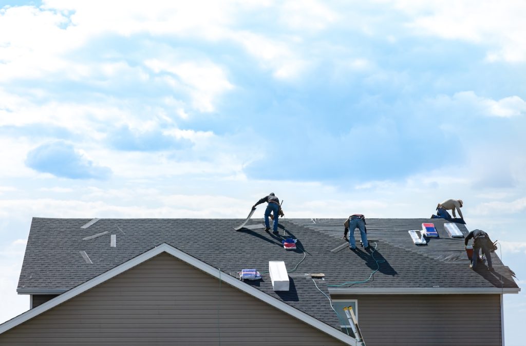 Roofing crew installing shingles on a Spokane home against a blue sky